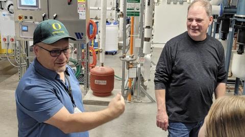 two men talk in front of machines